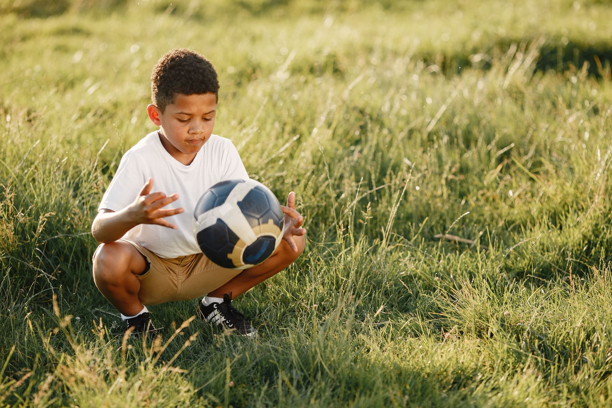 Young boy crouching in long grass holding a football