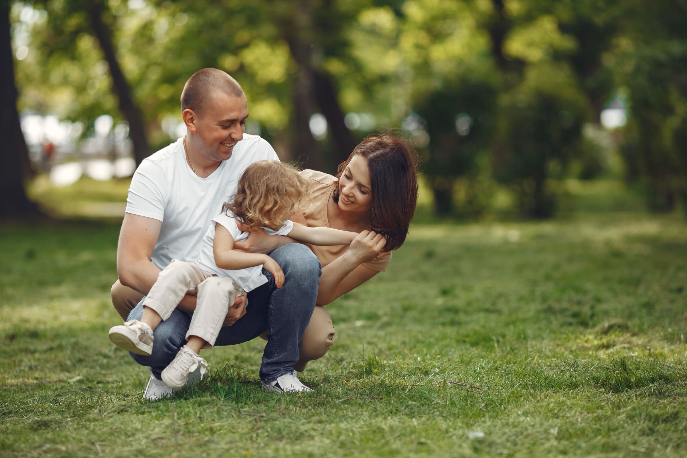 Parents crouching in a park with their young daughter